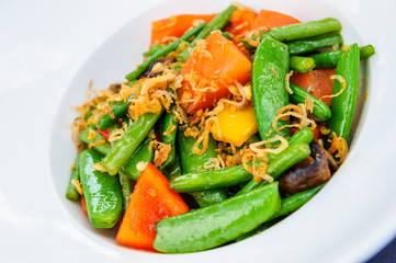 Plate of baked green beans mixed with pea pods and carrot