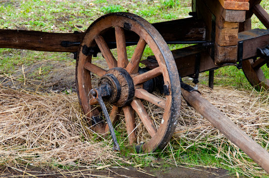 One very old wooden cart wheel against a background of straw.