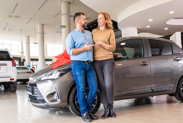 Fototapeta na wymiar Portrait of smiling adult couple standing in front of a vehicle after buying a new car at dealership.