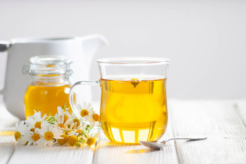 Cup of herbal tea with chamomile flowers and honey on the white wooden background. Natural organic alternative medicine