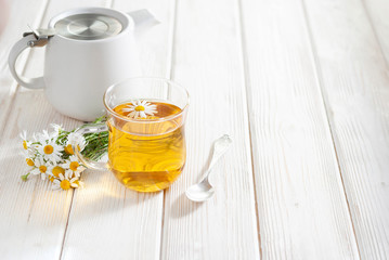Cup of herbal tea with chamomile flowers on the white wooden background. Natural organic alternative medicine concept