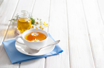Cup of herbal tea with honey and chamomile flowers on the white wooden background. Natural alternative medicine