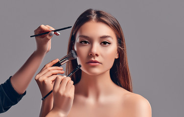 Cute attractive girl with makeup brushes isolated on gray background. Beauty salon, make-up.