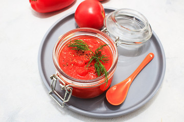 Ajvar (pepper mousse) in a jar and on gray plate and gray backgground. Ajvar - delicious dish of red peppers, tomato and garlic.