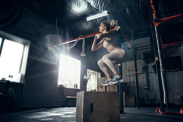 Jump box. Young caucasian female athlete training in gym, doing strength exercises, practicing. Beautiful girl works on her upper and lower body. Fitness, wellness, sport, healthy lifestyle concept.