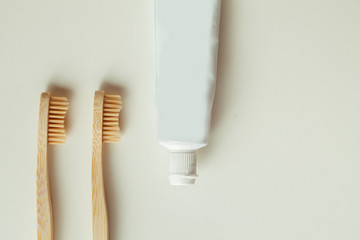 Two bamboo toothbrushes with toothpaste tube on the warm white background. flat lay with copy space