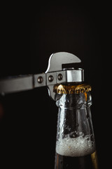 Upper part of the glass beer bottle with metal can opener on the black background