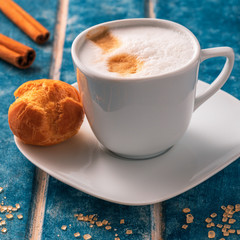 Cup of cappuccino, eclair, strawberries and cinnamon sticks on a background of blue wooden boards.