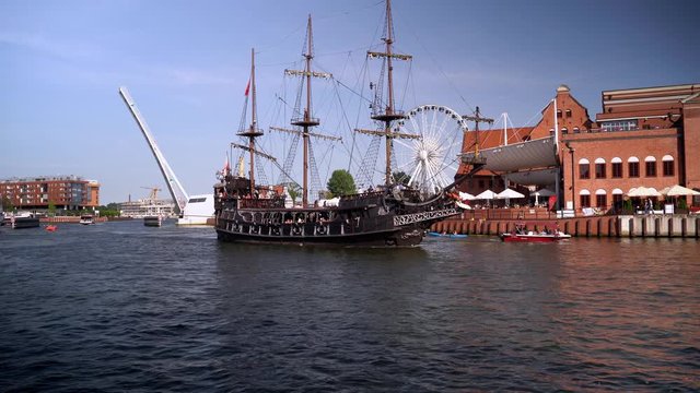Gdansk, North Poland : People doing leisure activities and black pirate ship sailing in motlawa river over a weekend at city center main square during sunset