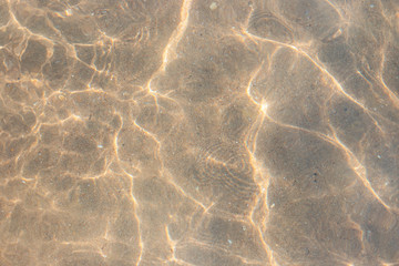 Fototapeta na wymiar clear sea water with waves and sun reflection on the sandy bottom. Water texture