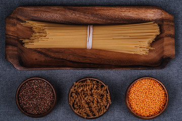 Pasta, wooden tray and legumes on gray background