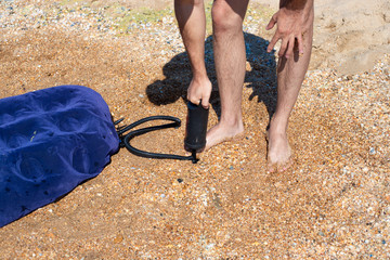 a man in swimming trunks pumps up a rubber mattress on the sand, on the seashore. Swimming on...