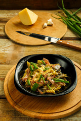 Black plate with pasta with ham and mushrooms in a creamy sauce on the table with a fork on the board.