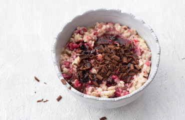 Delicious oatmeal porridge with butter, jam and grated chocolate in gray bowl on light gray background. healthy homemade breakfast. selective focus, space, top view