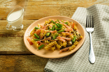 a plate of pasta with ham and mushrooms in a creamy sauce on the table with a fork on a napkin.
