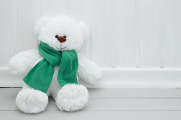 Child's toy white teddy bear with green scarf sitting on the floor. Copy space.