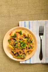 a plate of pasta with ham and mushrooms in a creamy sauce on the table with a fork on a napkin on the tablecloth.