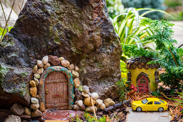 Secluded Fairy Garden door entrance in rock flanked by smaller fairy house with car parked in front

