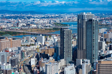 Obraz premium Japan. Panorama of Osaka from a height. Skyscrapers, apartment buildings, and the Yodo river. A big city under a blue sky. Osaka against the silhouettes of mountains. Urban landscape.