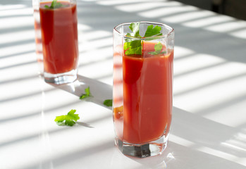 red tomato juice in glass glasses with parsley leaves. the shadow of the blinds on the windows falls on the table