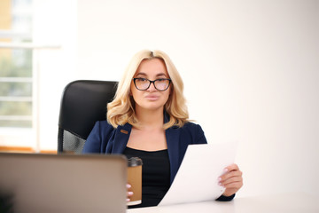 smiling blonde businesswoman with glasses using laptop in the office