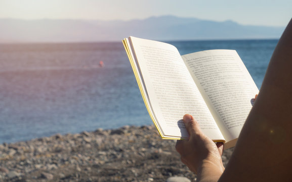Woman hands holding book on beach