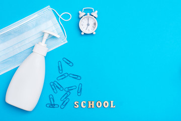 Back to school. Social distancing. Alarm clock, wooden letters, protective mask and sanitizer on a blue background
