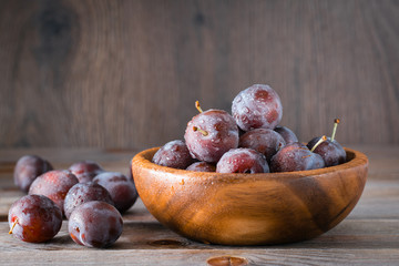 Obraz premium Ripe blue plum in a wooden plate on the table. Autumn harvest. Rustic style. Copy space