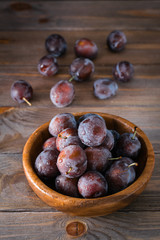 Ripe blue plum in a wooden plate on the table. Autumn harvest. Rustic style. Healthy eating