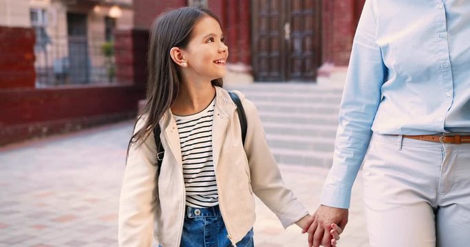Portrait of Caucasian cute happy schoolgirl walking and chatting with woman after school outdoors. Cheerful teen female junior student speaking with mother with smile on face. Talk concept