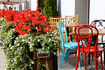 Fototapeta na wymiar Street cafe in a city, tables and vintage metal chairs in a restaurant outdoor. Pots with flowers, elegant setting for celebration and date