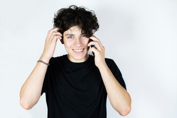 A handsome teenage boy smiles and talks on the phone, the guy has happy emotions on his face. The guy has curly hair and white healthy teeth