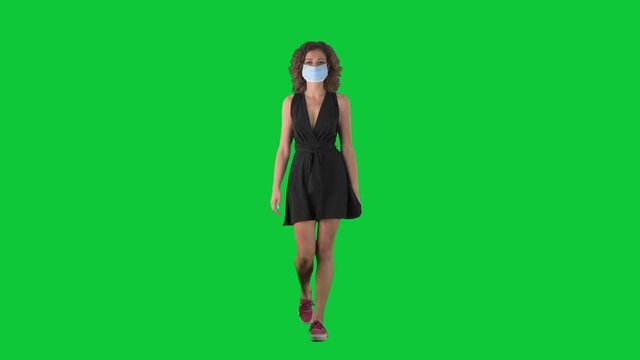 Young woman walking wearing then removing face mask against corona virus on green screen chroma key background. 