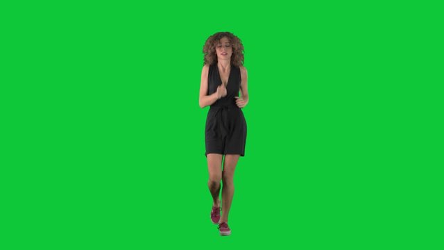 Slow motion of worried young pretty woman in dress jogging in hurry on green screen chroma key background. 