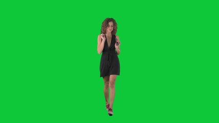 Happy young woman dancing while walking and singing music on her cell phone on green screen chroma key background. 