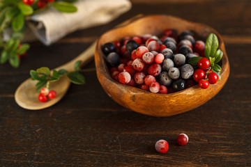 frozen cranberries and blueberries in a wooden bowl, decorated with a sprig of fresh cranberries.on a dark wooden background. Close-up, blurred background
