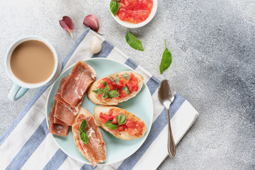 bruschetta, toast with sliced tomatoes, jamon and Basil on a blue plate, and coffee with milk in a blue Cup. copy space. flatly