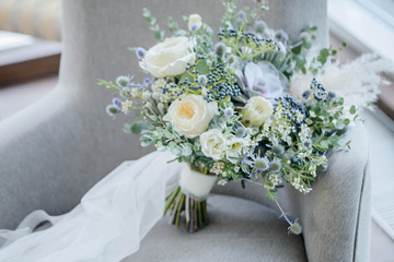 Bridal bouquet. The bride's bouquet. Beautiful bouquet of white, blue flowers and greenery, decorated with long silk ribbon lies on a gray textural background