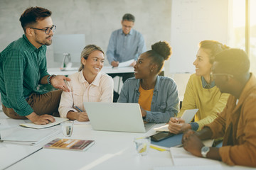 Obraz premium Happy college friends talking while studying and using laptop in the classroom.