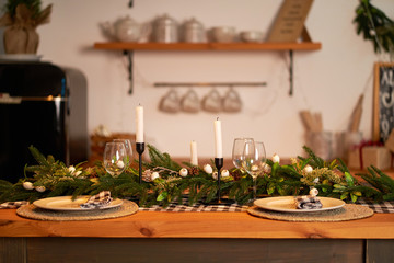The festive Christmas table is decorated with branches of a Christmas tree, candles and garlands. Cozy home Christmas atmosphere.