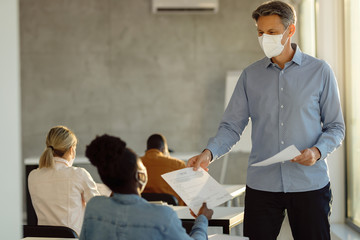 Happy professor wearing face mask while giving his students exam results.