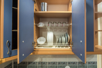 set of plates, cups, knives, forks and wine glasses on the shelf in the kitchen cabinet