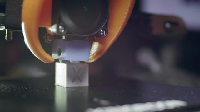 The 3D printer prints an abstract cube shape from white abs plastic. 3D printer head in action. An automatic three-dimensional 3d printer performs plastic. Macro