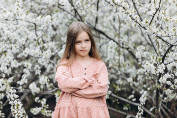 A little child girl stands with her arms folded on her chest and looks with a satisfied expression on her face.