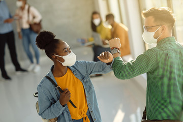 Happy university students greeting with elbow while wearing protective face masks.