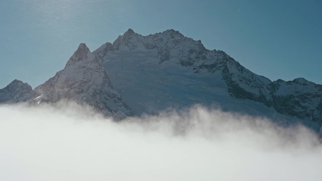 Snow capped mountains above clouds in a blue sky in sunny weather