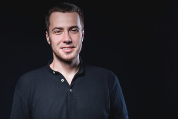 Obraz premium Portrait of an emotional handsome young man, on a black background in the studio, who stands in a brooding pose. Expression of emotions and feelings