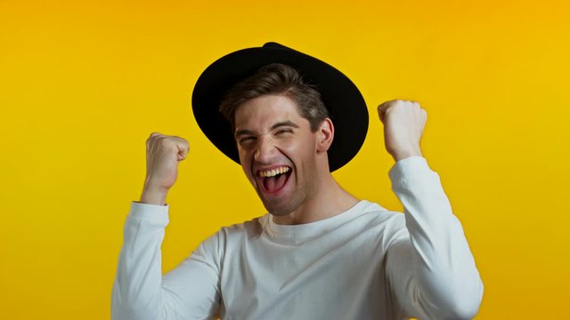 Yes winner gesture. Amazed european hipster man shocked. Handsome guy in hat surprised to camera over yellow background
