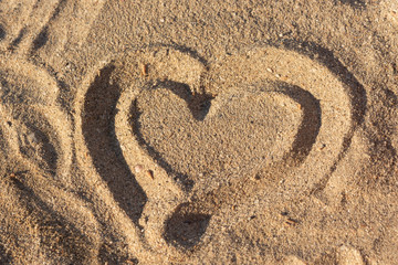Fototapeta na wymiar Heart on the sand as a symbol of love. The view from the top on the hot sand. Hand-drawn heart shape on the beach. Love and unity. Dreams of the sea and vacation.