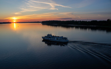 A small boat floats on the river against the background of the sunset.